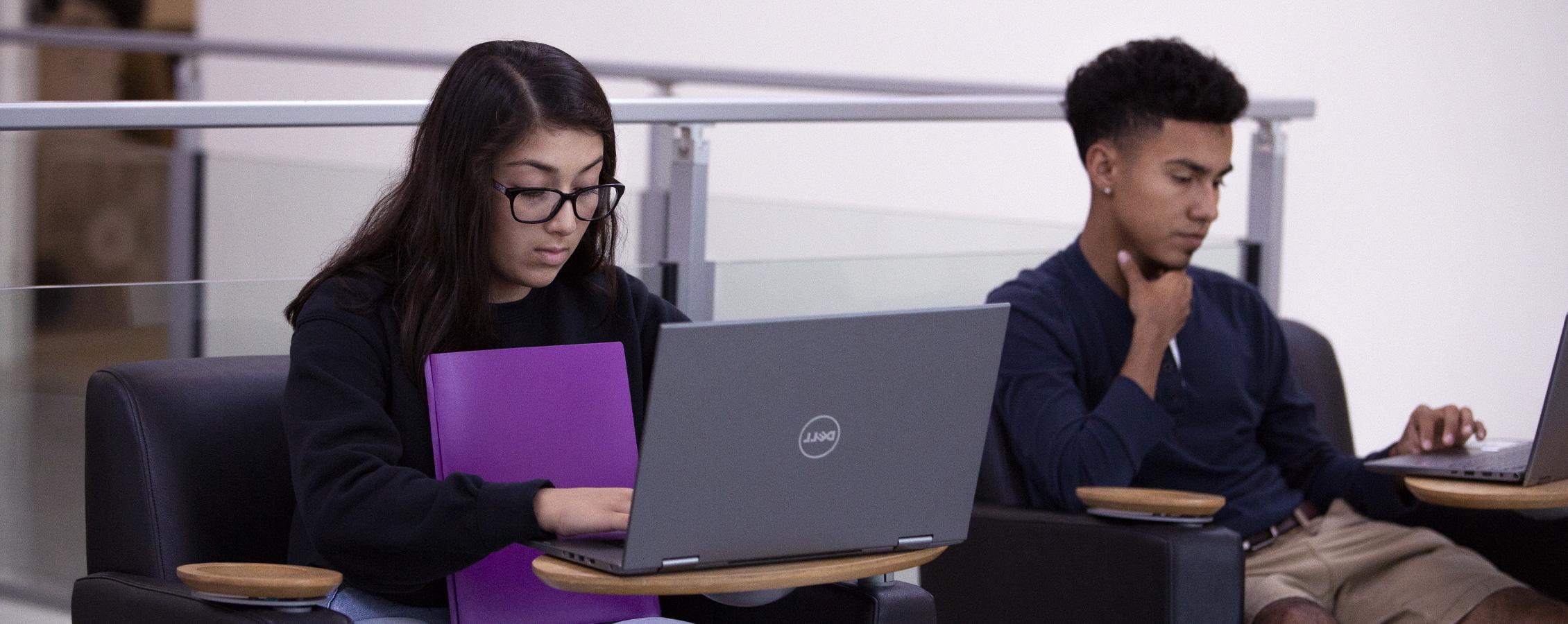 在会议区使用笔记本电脑的两名学生.